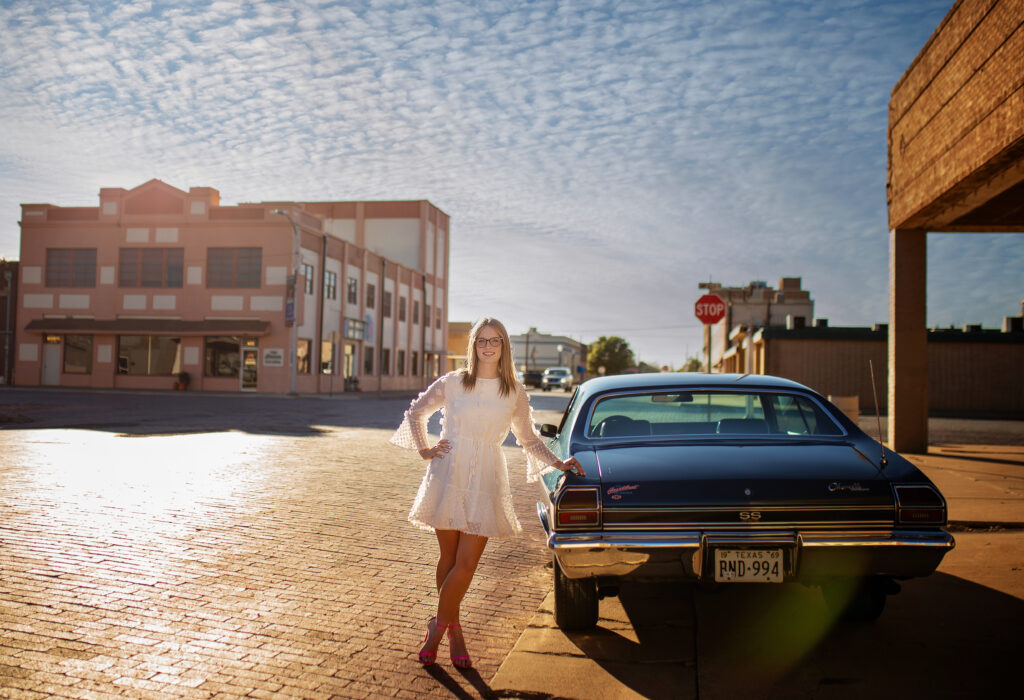 High School senior standing next to a blue Chevelle in downtown plainview. 
