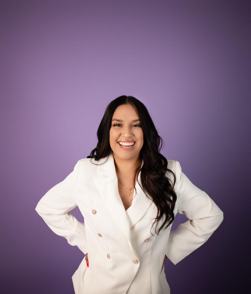College grad laughing in white outfit with a purple seamless background
