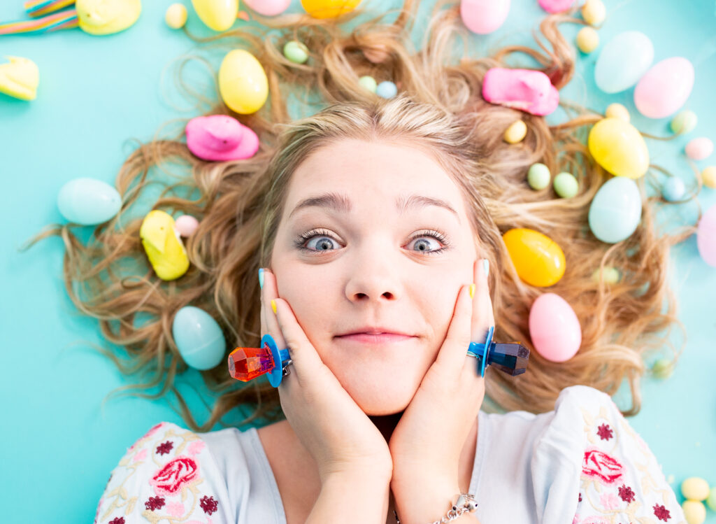 high school senior girl laying in a pile of candy for Easter. With ring pops on and against her face. 