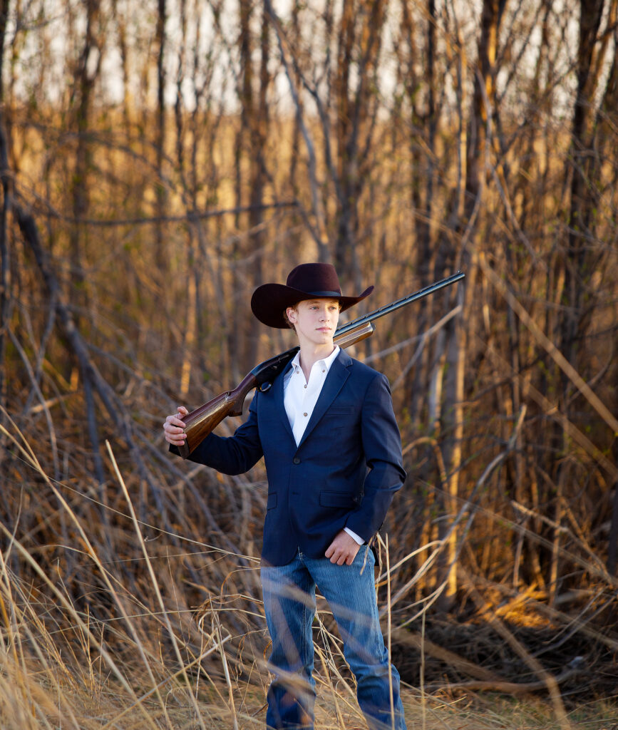 Senior boy standing in a field holding his grandpas shotgun 