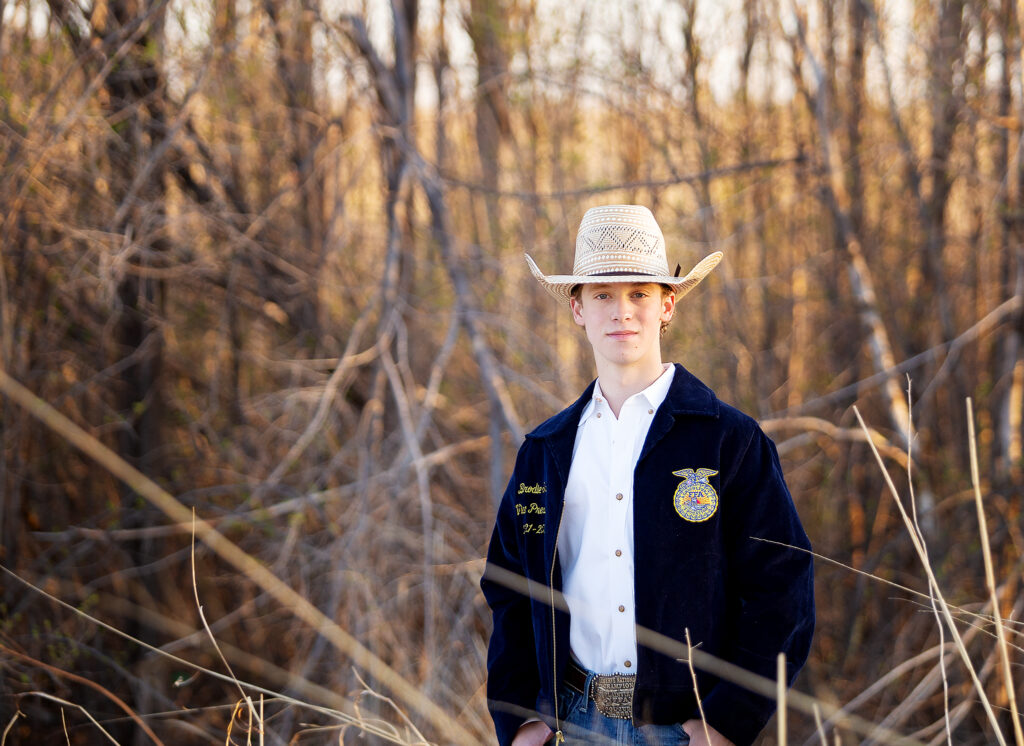 Plainview High school senior boy standing in a field while wearing his FFA jacket 